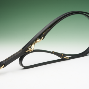 A black leather dog lead, with brass hardware, lies looped on a white surface against a faded dark green background.